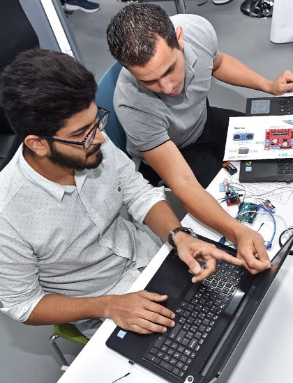 A trainer guiding a participant at a laptop during the Studio 5 Training of Trainers